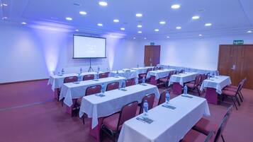 Una sala de conferencias con varias mesas, sillas y una pantalla para proyector.