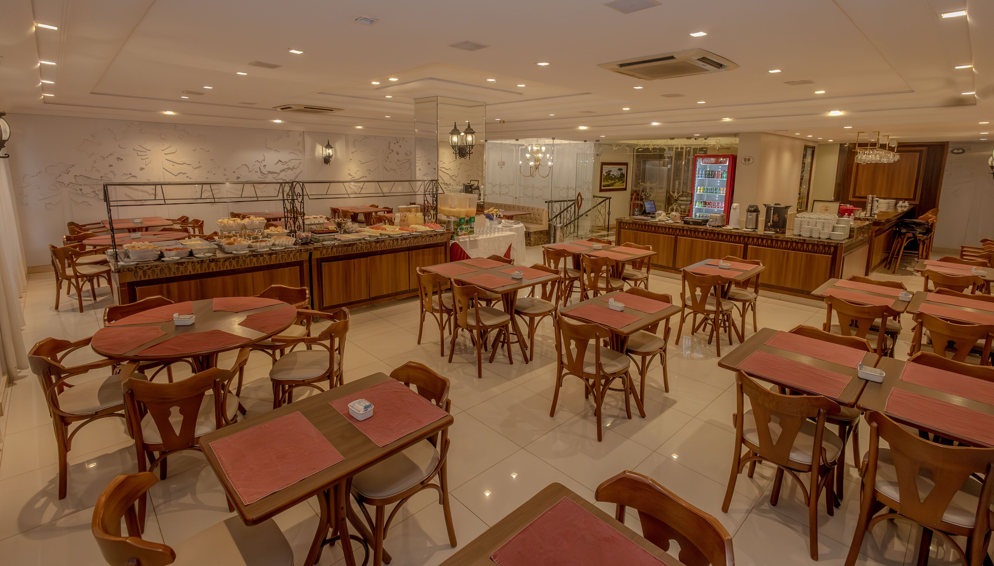 A spacious dining area with multiple tables and chairs, a buffet station, and a Coca-Cola refrigerator.