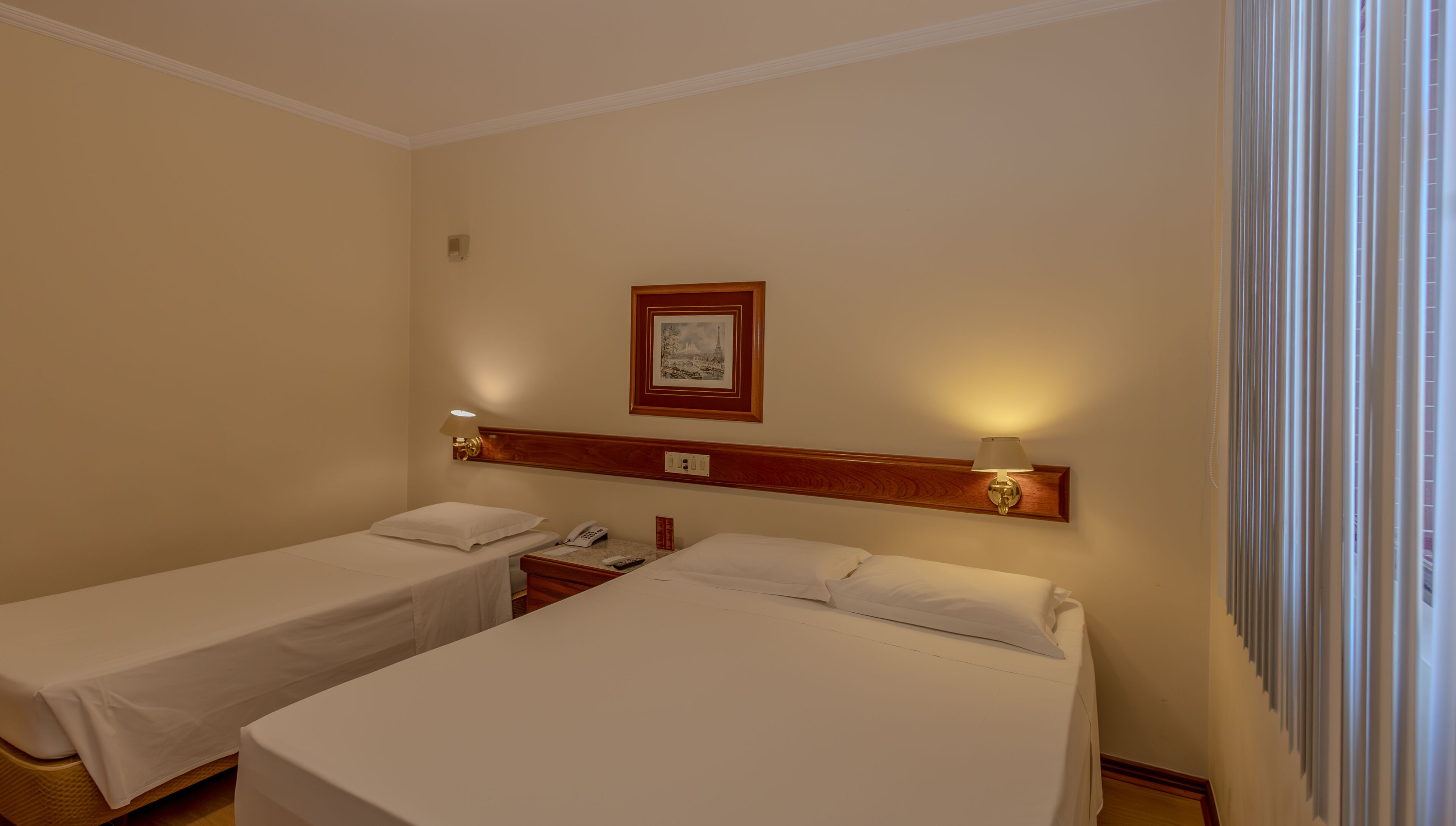 Habitación de hotel con dos camas individuales, una mesita de noche con lámpara, un teléfono y un cuadro en la pared.