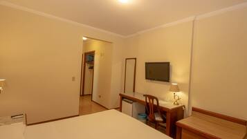 Habitación de hotel con cama, escritorio, silla, televisor y un refrigerador pequeño.