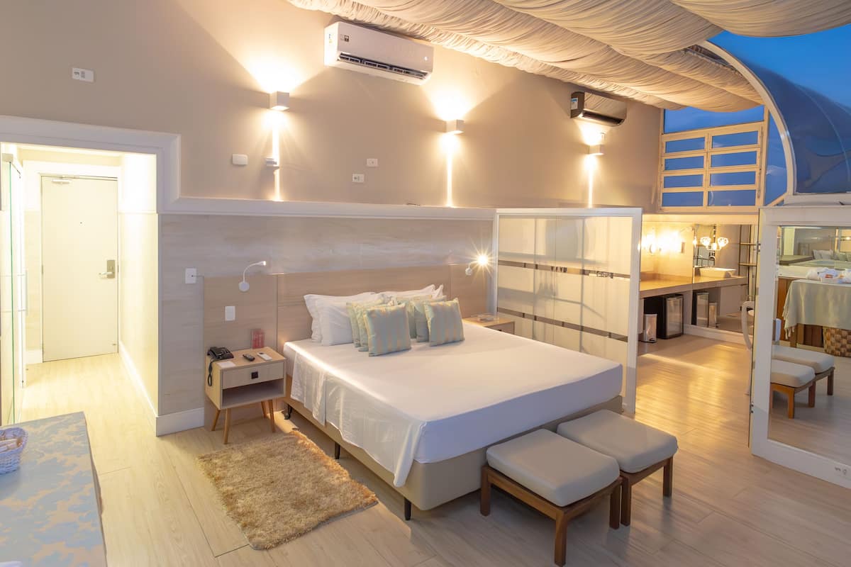 A modern bedroom with a large bed, bedside tables, a nightstand, a bench, and a view of the bathroom.