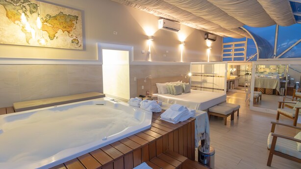 A modern, well-lit bedroom with a large bed, a separate seating area, and a hot tub. - Lizon Curitiba Hotel (Curitiba)
