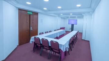 A conference room with a long table, chairs, a TV screen, and a door marked "SAÍDA".