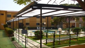 A covered outdoor area with a pool, seating, and a building in the background.