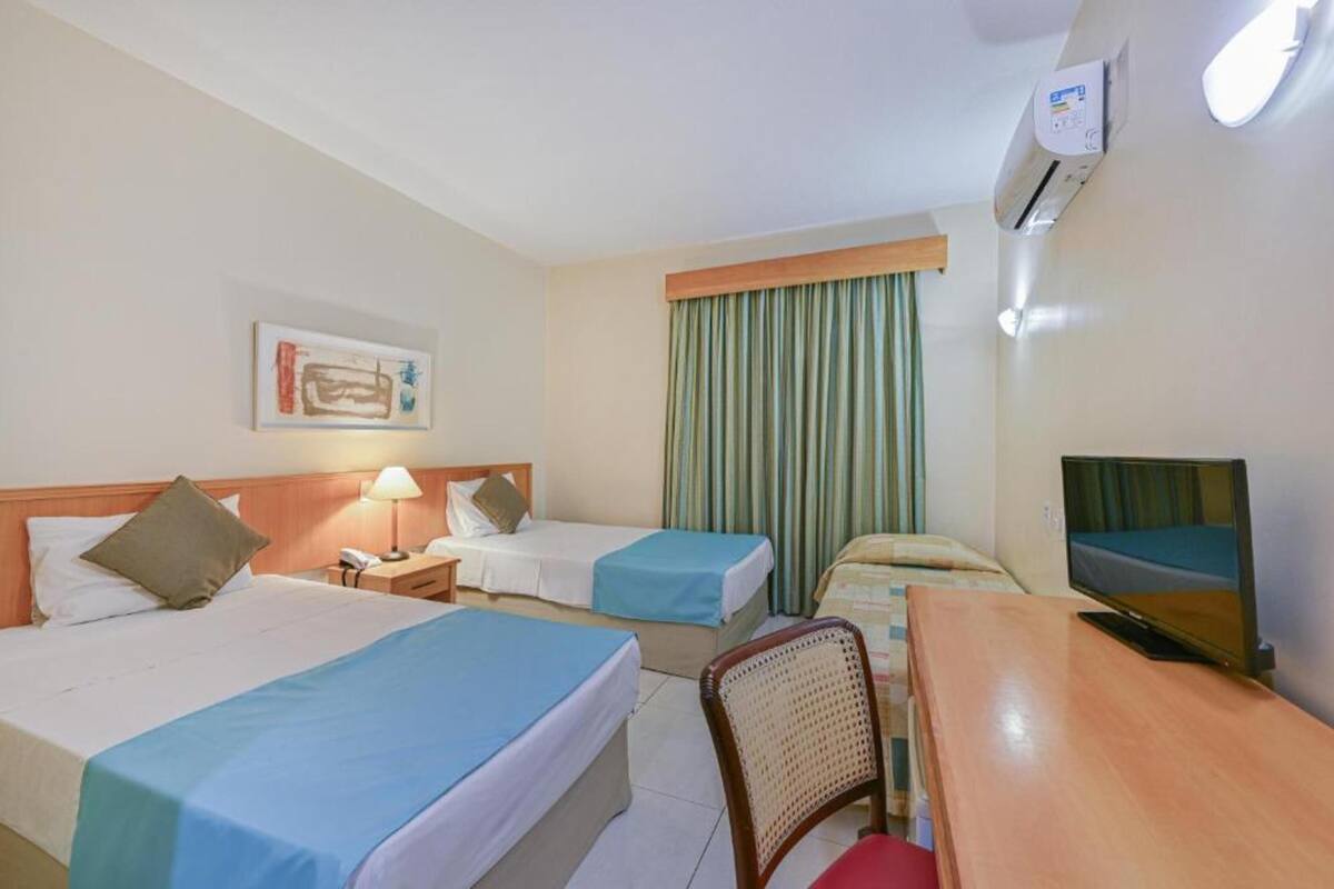 Habitación de hotel con dos camas, un escritorio, una silla, un televisor, un equipo de aire acondicionado y una cortina.