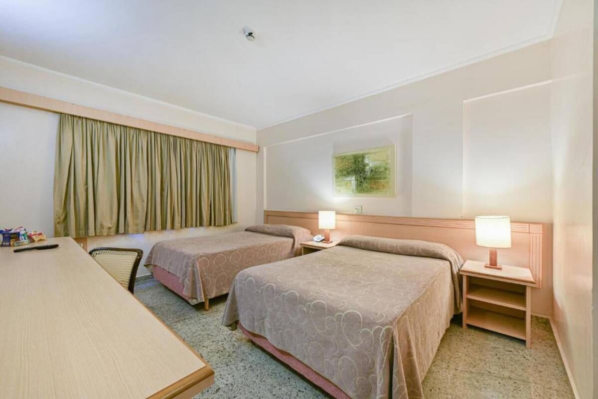 Una habitación de hotel con dos camas, un escritorio, una silla y un cuadro en la pared.