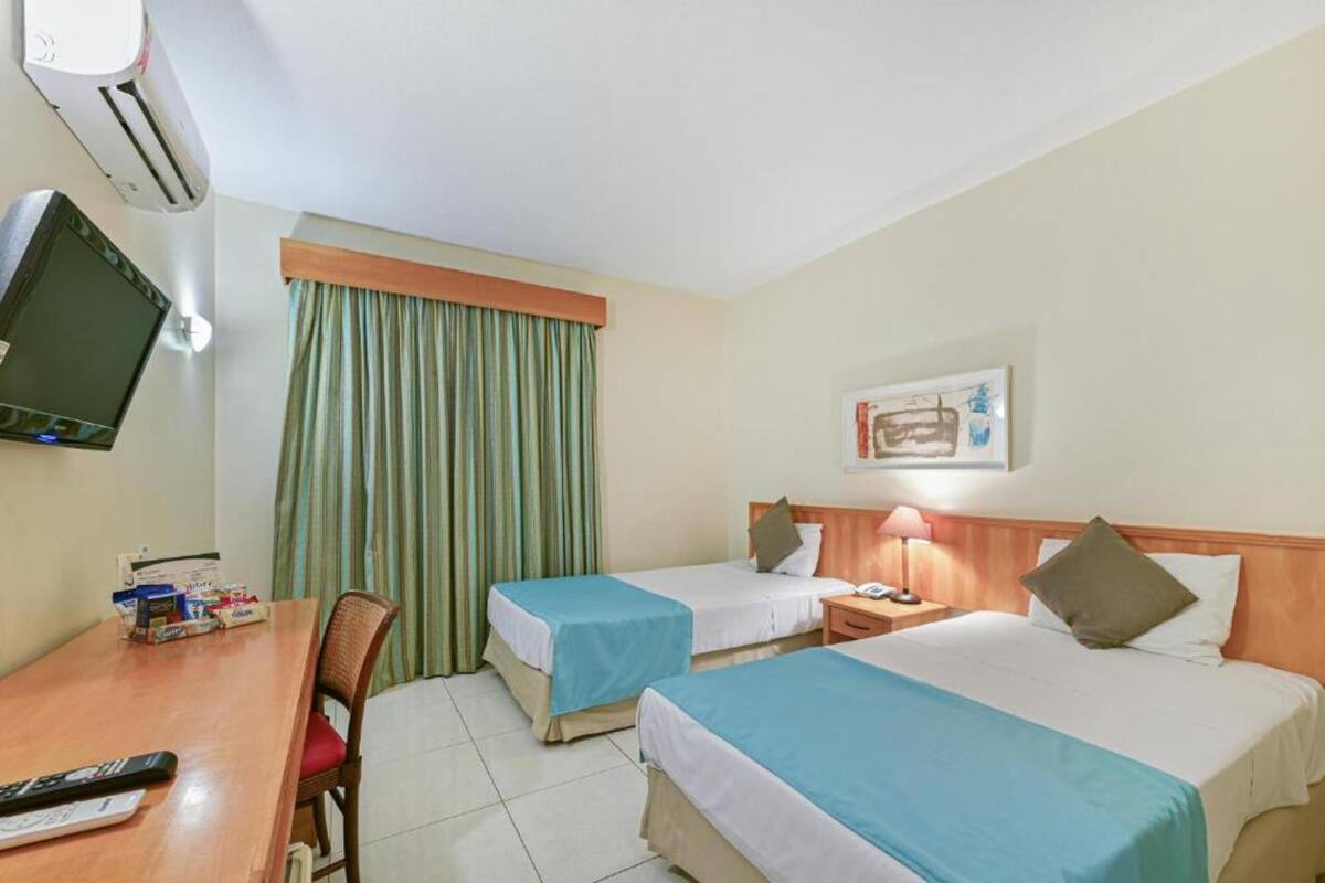 Habitación de hotel con dos camas, un escritorio con una silla, un televisor y una ventana con cortinas.