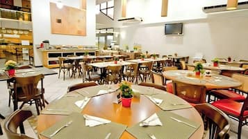 Un comedor amplio con varias mesas redondas, sillas y plantas en macetas.