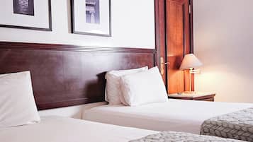 A hotel room with two beds, a wooden headboard, a nightstand with a lamp, and two framed pictures on the wall.