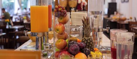 Un bufé de desayuno con diversas frutas, jugos y una máquina de café.