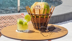 A table with a glass of a lime-based drink, a basket with a coconut and a straw, and a pair of sunglasses. - Metropolitan Hotel (Teresina)