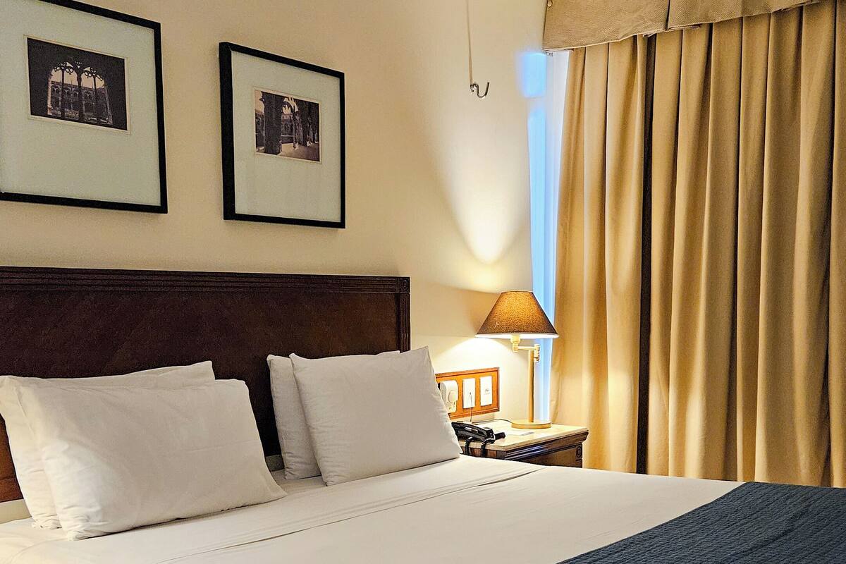 A hotel room with a large bed, a nightstand, a lamp, and two framed pictures on the wall.