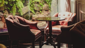 A room with a glass door leading to a garden, featuring two leather chairs and a small round table. - Metropolitan Hotel (Teresina)
