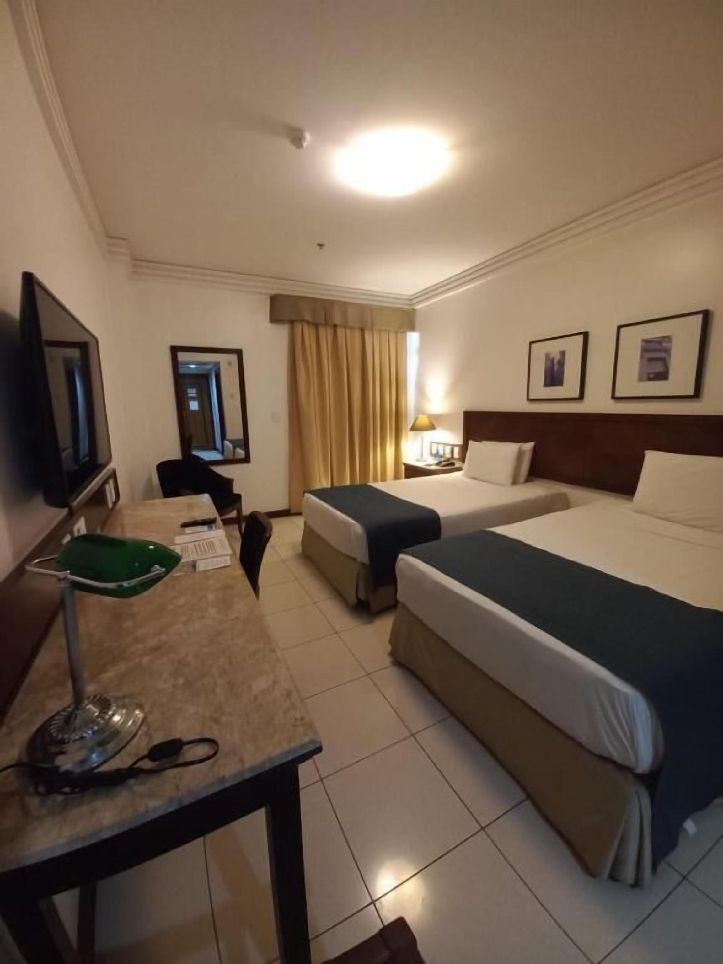 A hotel room with a bed, a desk with a chair, a television, and a window with curtains.