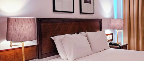 A hotel room with a large bed, two bedside tables, a nightstand, a lamp, and two framed pictures on the wall.