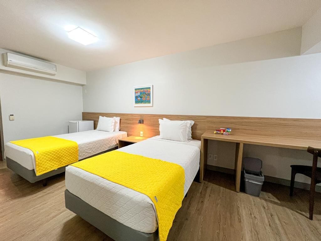 A hotel room with two beds, a desk, and a trash bin.