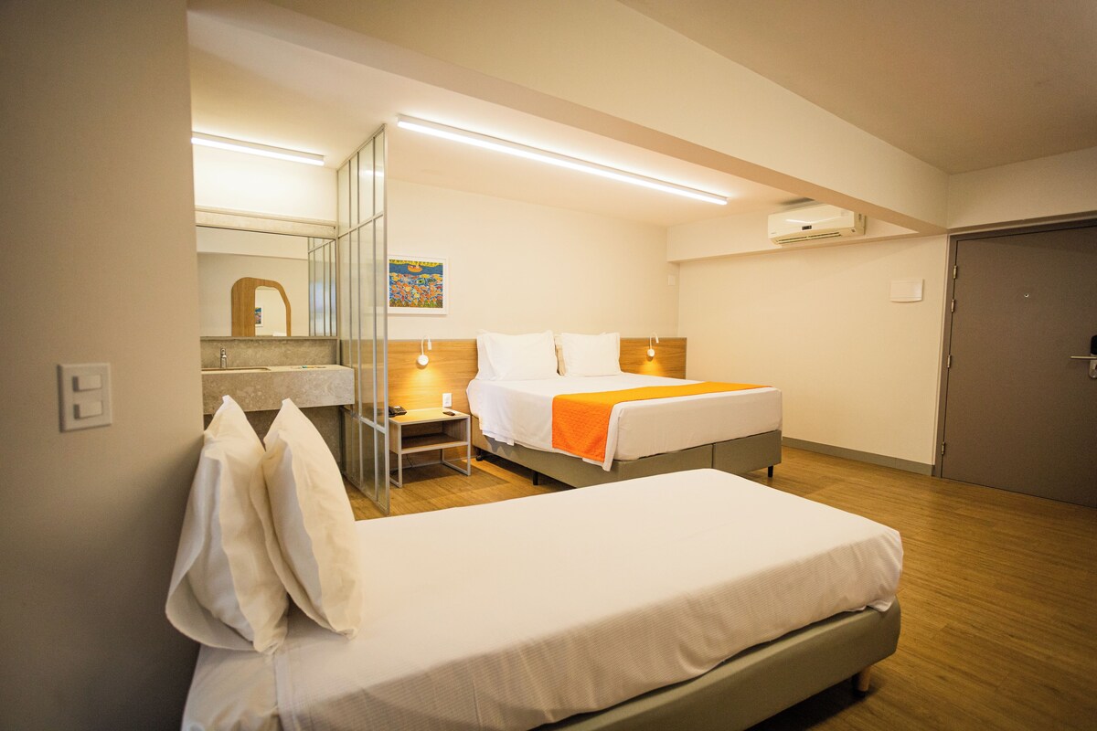 A hotel room with a bed, bedside table, and a mirror.