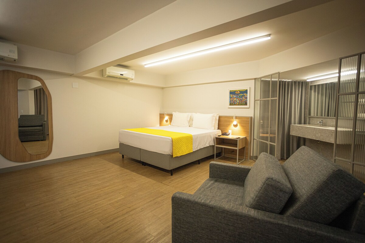 A hotel room with a bed, a sofa, a desk, and a bathroom.
