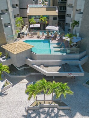 A rooftop pool with lounge chairs and palm trees, surrounded by modern buildings. - San Marino Suite Hotel (Maceió)