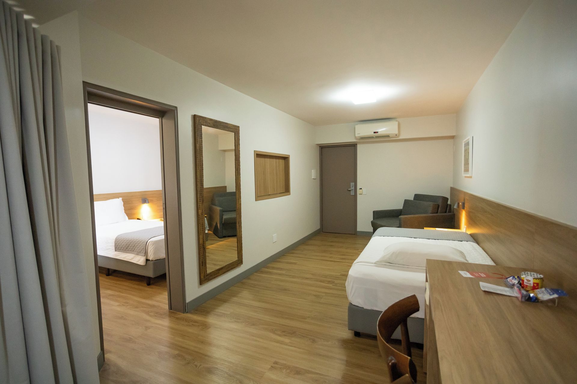 A hotel room with two beds, a desk, a chair, a wardrobe, and a mirror.