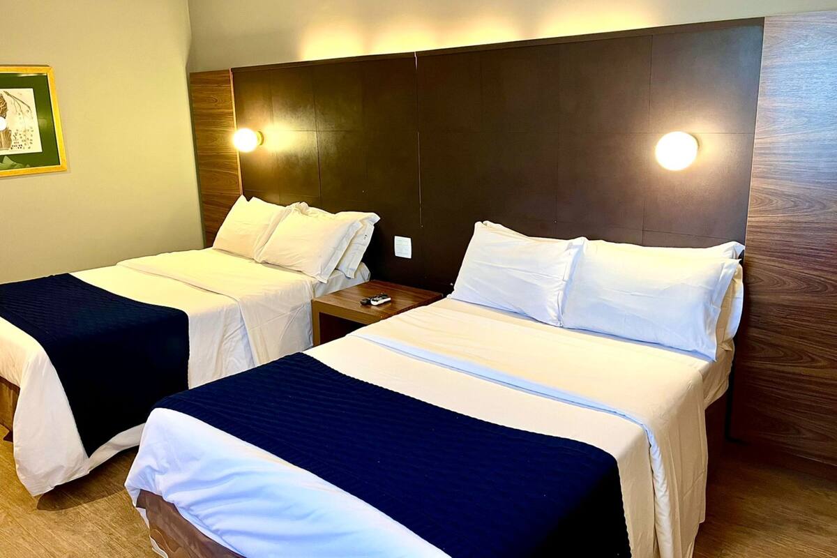 Camera d'albergo con due letti, un comodino e una lampada a parete.