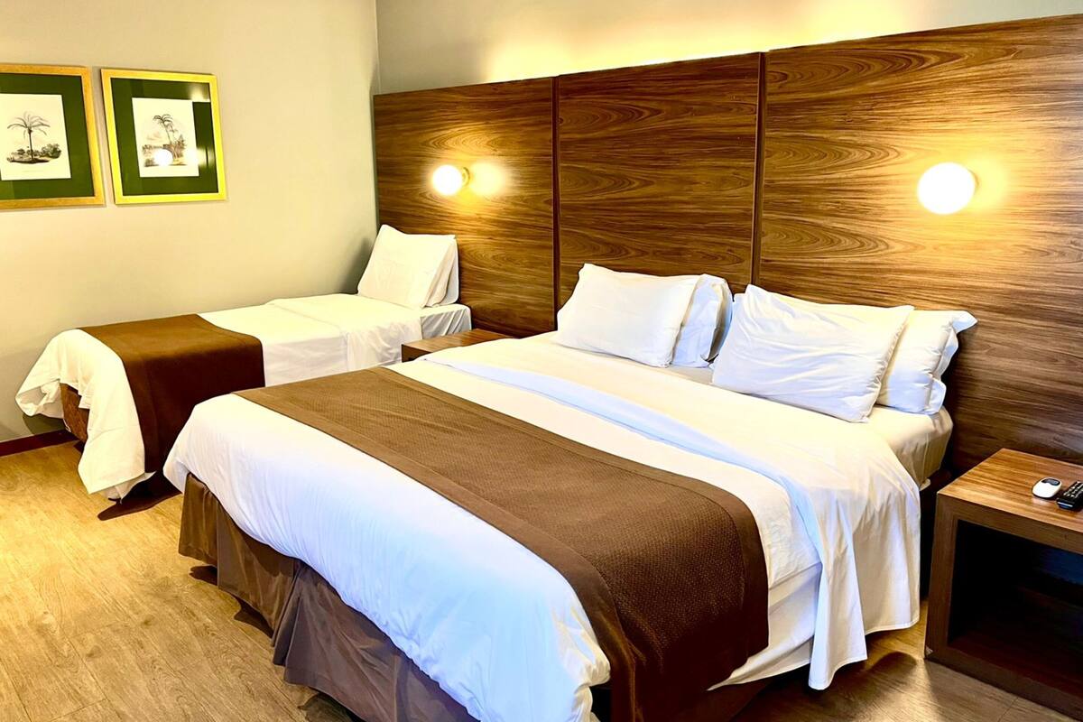 Una camera d'albergo con due letti, una testiera in legno, lampade sui comodini e quadri appesi al muro.
