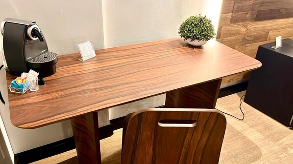 Una mesa de madera con una cafetera, una pequeña planta en maceta y algunos objetos encima.