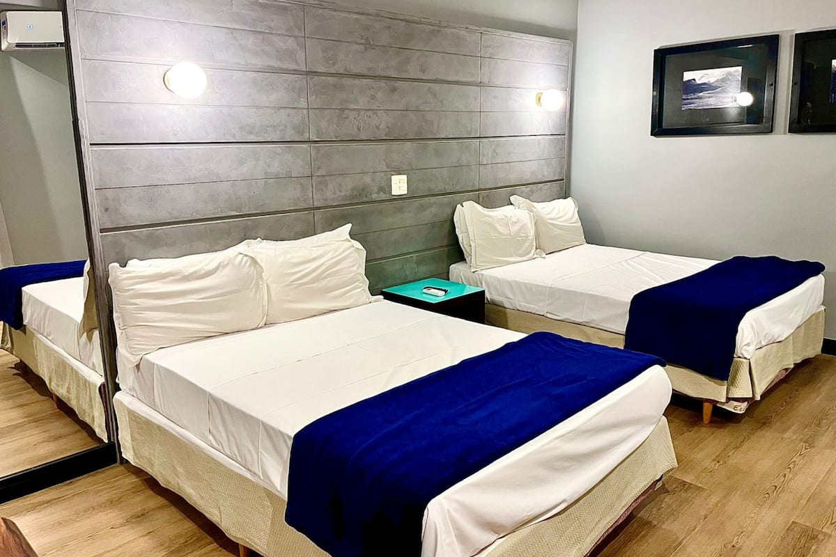 Una camera d'albergo con due letti, una testiera grigia, un tavolino e un quadro appeso al muro.