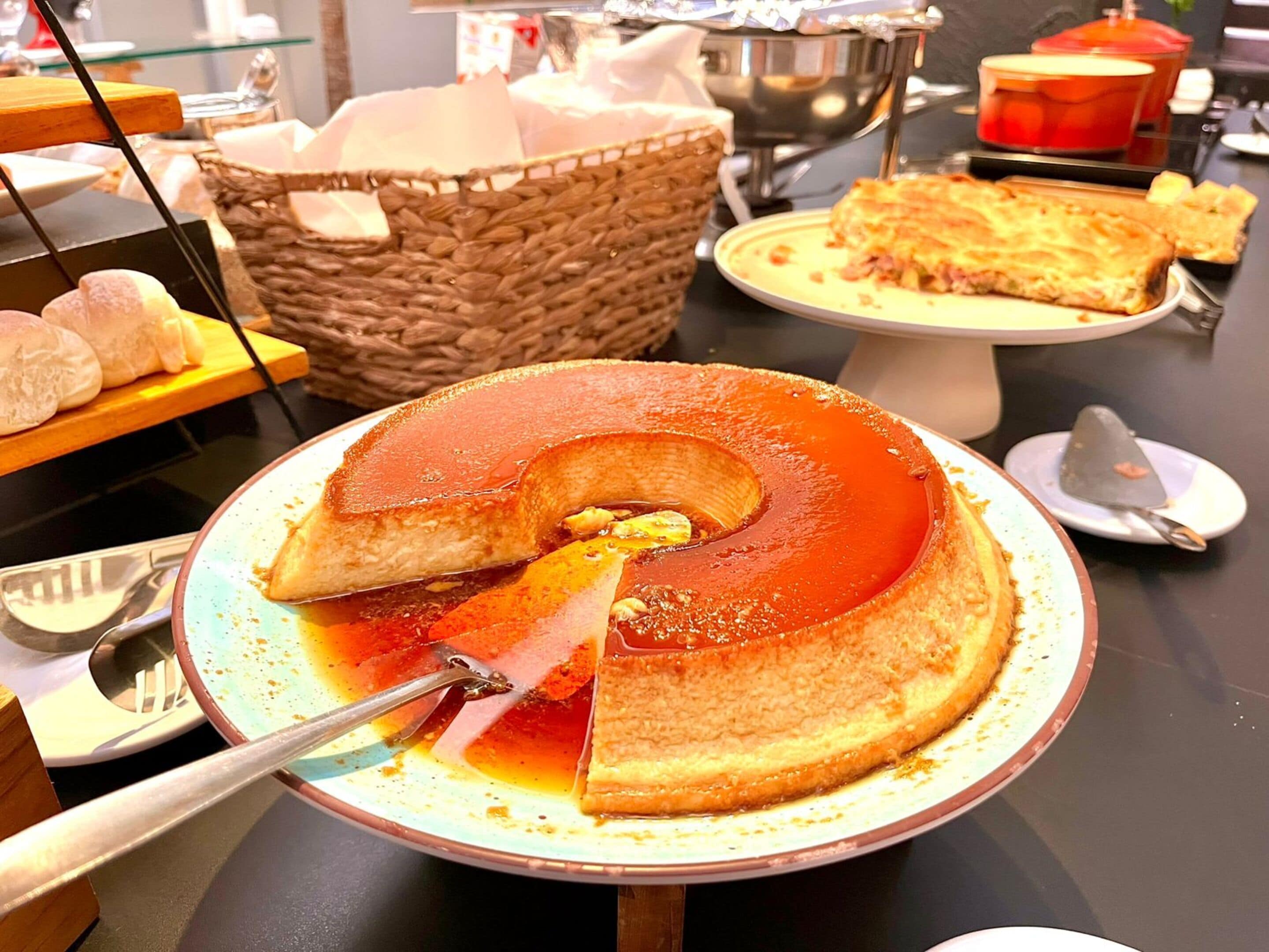 Un présentoir à desserts avec un flan au caramel, une part étant servie, et un panier à pain en arrière-plan.