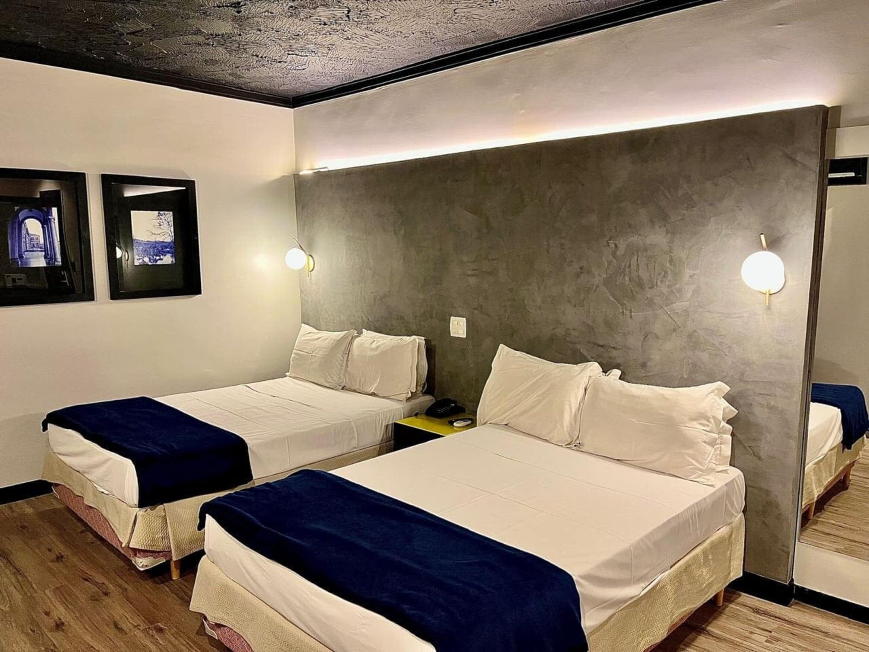 A hotel room with two beds, a large mirror, and wall-mounted light fixtures.