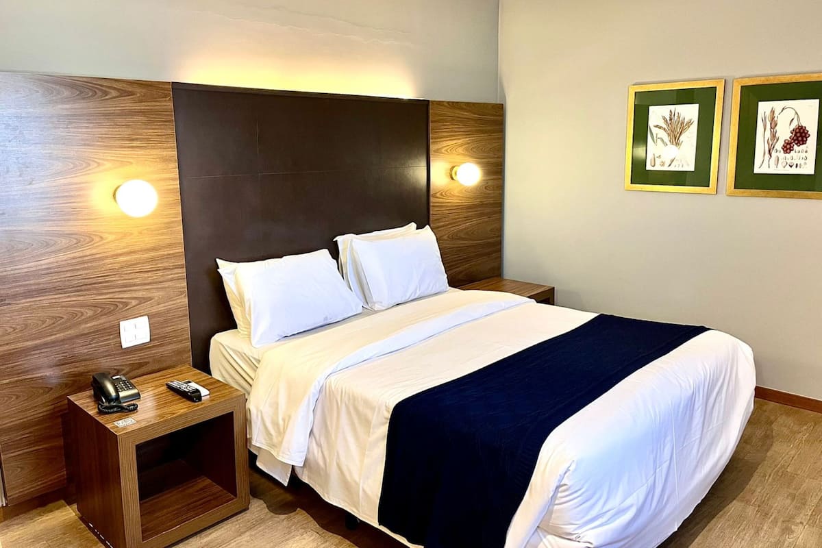 Camera d'albergo con un letto grande, una testiera in legno, comodini con telefoni e un'opera d'arte botanica incorniciata appesa al muro.