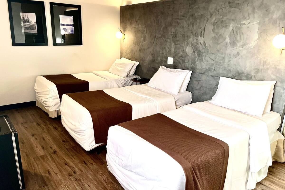 Camera d'albergo con due letti, pavimento in legno, parete grigia e strutturata e due quadri appesi al muro.
