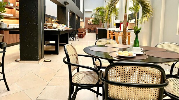 A modern dining area with round tables, wicker chairs, and a central island with a coffee machine. - Oasis Tower Hotel (Ribeirão Preto)