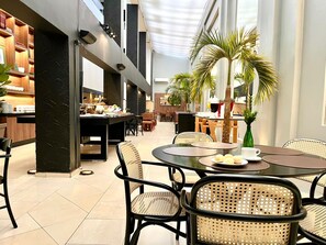 A modern dining area with round tables, wicker chairs, and a central island with a coffee machine. - Oasis Tower Hotel (Ribeirão Preto)