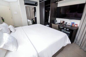 A hotel room with a large bed, a desk with a computer, a TV, and a minibar. - Royal Collection Paulista (São Paulo)