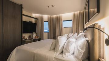 A hotel room with a large bed, a desk with a chair, a flat-screen TV, and a window with curtains.
