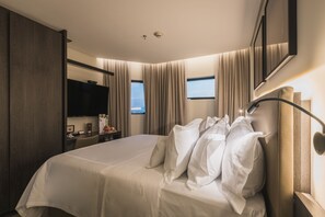 A hotel room with a large bed, a desk with a chair, a flat-screen TV, and a window with curtains. - Royal Collection Paulista (São Paulo)
