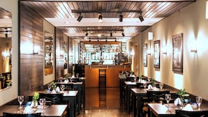A restaurant with a long, narrow layout featuring multiple tables and chairs, a central bar area, and a polished floor.