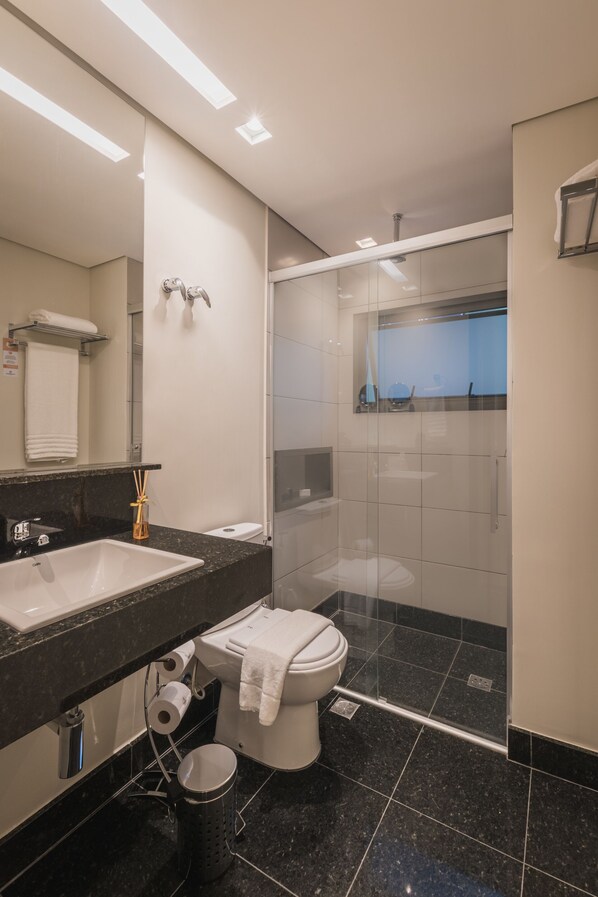 Un baño moderno con lavamanos de mármol negro, inodoro blanco y ducha con mampara de vidrio.