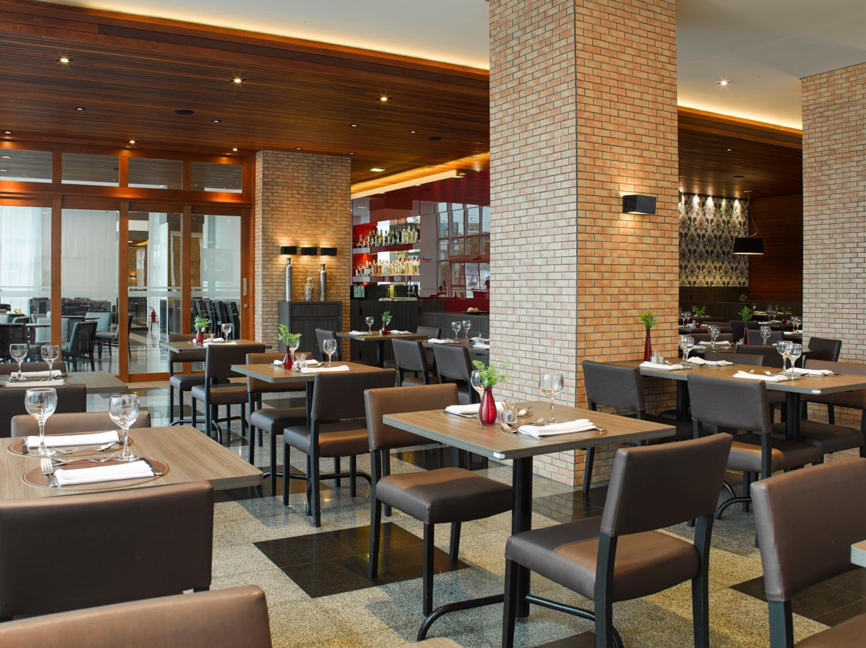 Een modern restaurant met bakstenen muren, een houten plafond en meerdere eettafels met stoelen.