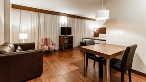 Une chambre d’hôtel moderne avec une table à manger en bois, un canapé en cuir et un téléviseur à écran plat.