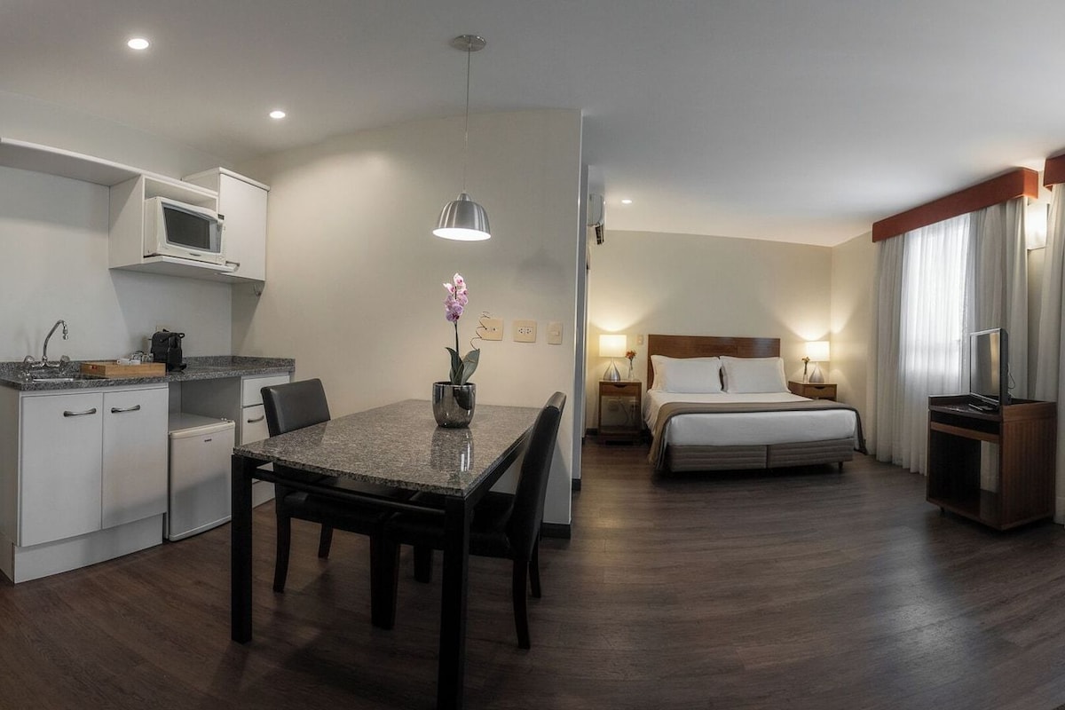 Ein Hotelzimmer mit Bett, Schreibtisch mit Stuhl, Fernseher, Lampe und einem Fenster mit Vorhängen.