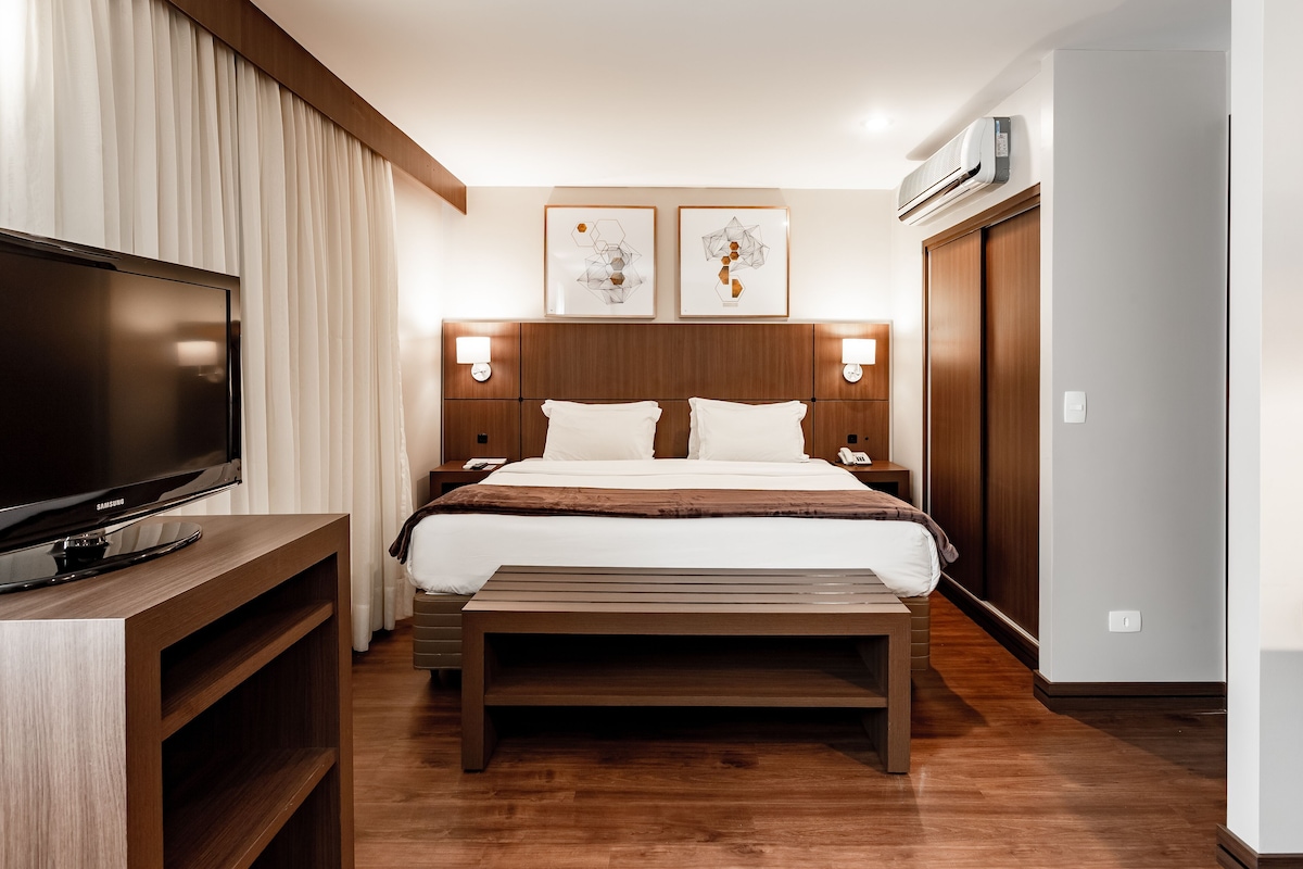Ein Hotelzimmer mit Bett, Nachttischlampen, Fernseher, Wandbild und Kleiderschrank.