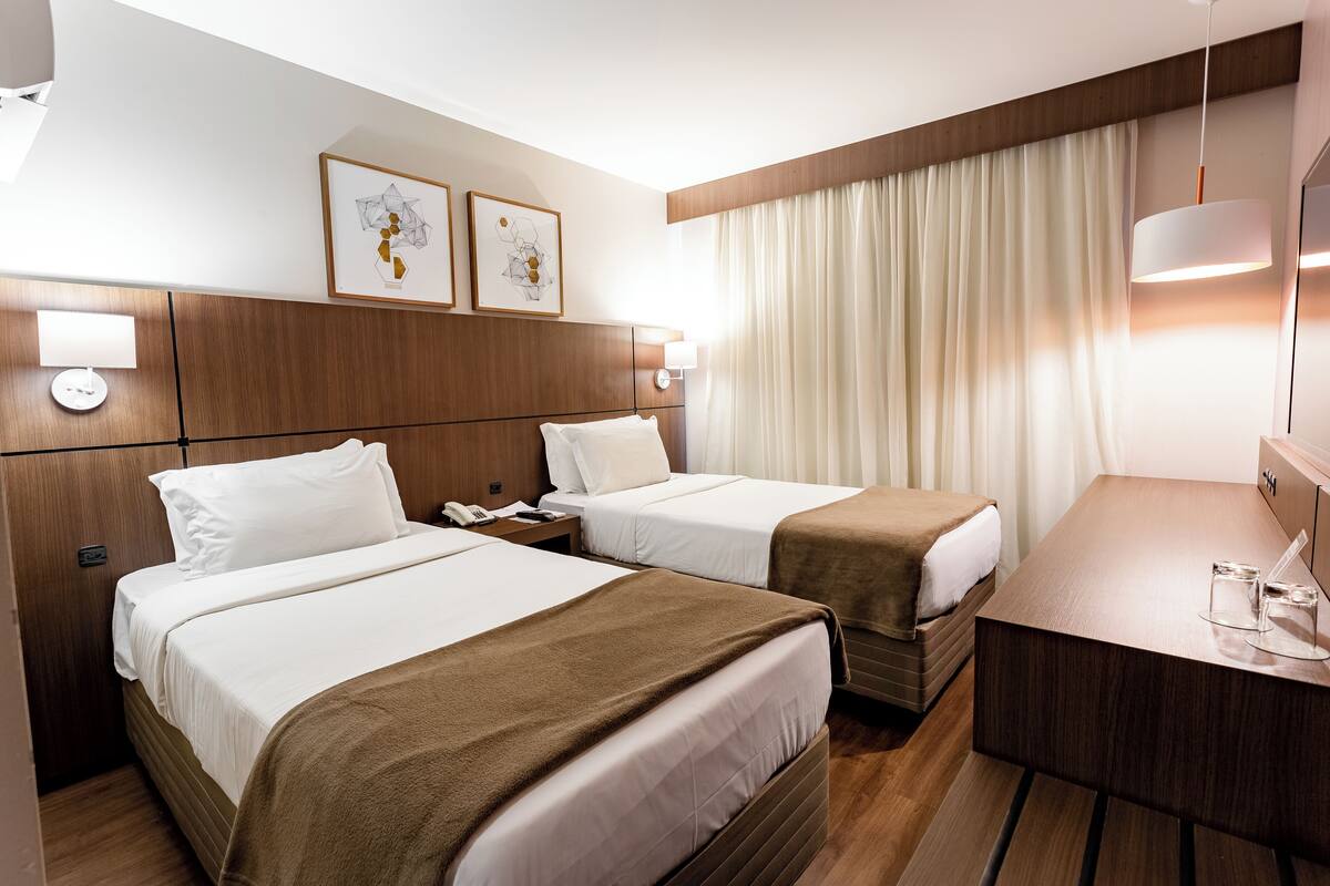 Une chambre d’hôtel avec deux lits, un bureau, une lampe et des œuvres d’art accrochées au mur.