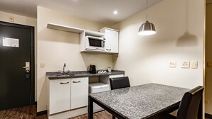 Une cuisine compacte équipée d’un four à micro-ondes, d’un évier et d’un petit réfrigérateur. On y trouve une table à manger avec des chaises, et une suspension lumineuse au-dessus.