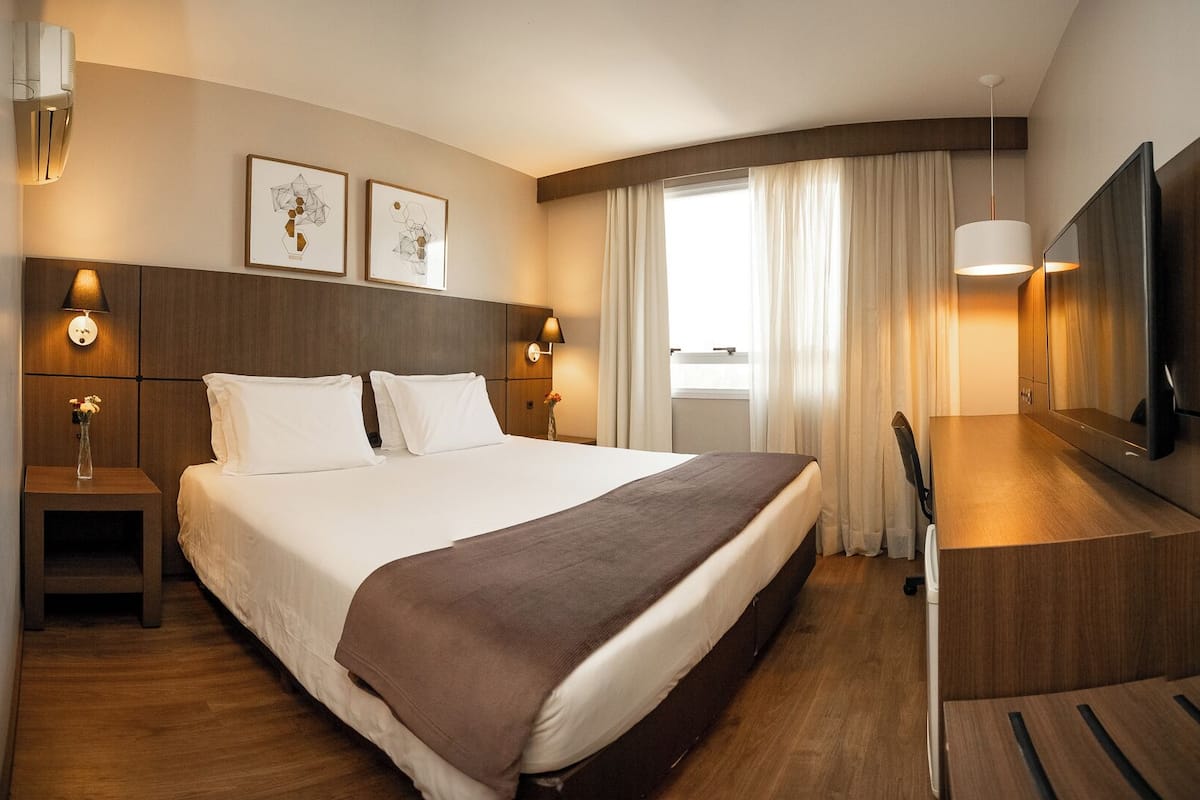 Une chambre d’hôtel moderne dotée d’un grand lit, de tables de chevet, d’un bureau et d’un téléviseur à écran plat.