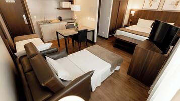 A compact hotel room with a sofa, a bed, a desk with a chair, a microwave, and a TV.