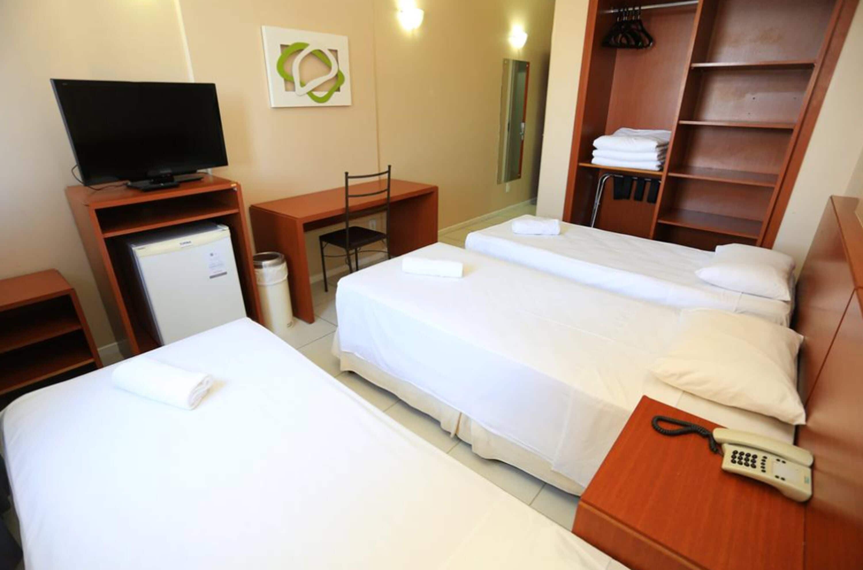 Een hotelkamer met twee bedden, een bureau met een computer, een televisie, een kledingkast en een telefoon.