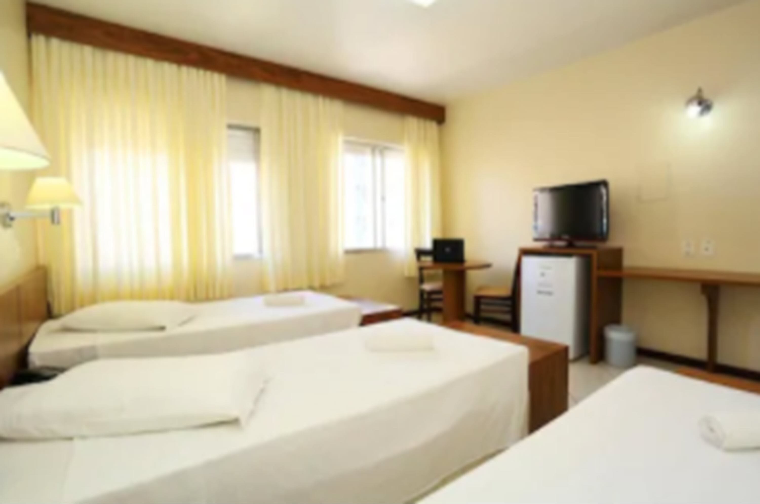 A hotel room with two beds, a desk with a television, and a small kitchenette.