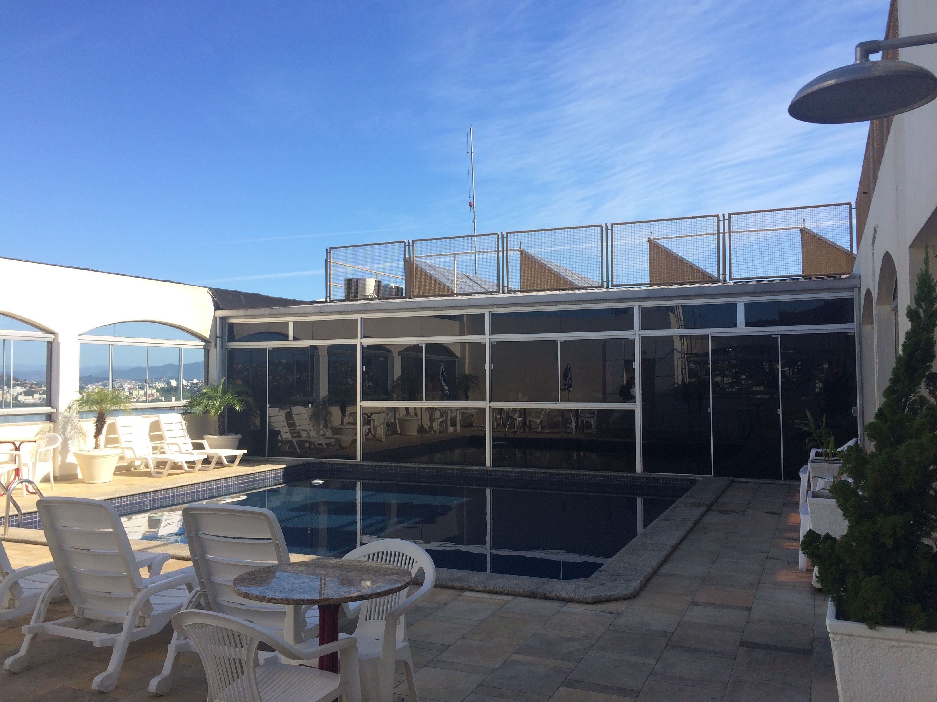 A rooftop pool area with lounge chairs and a glass-enclosed patio.